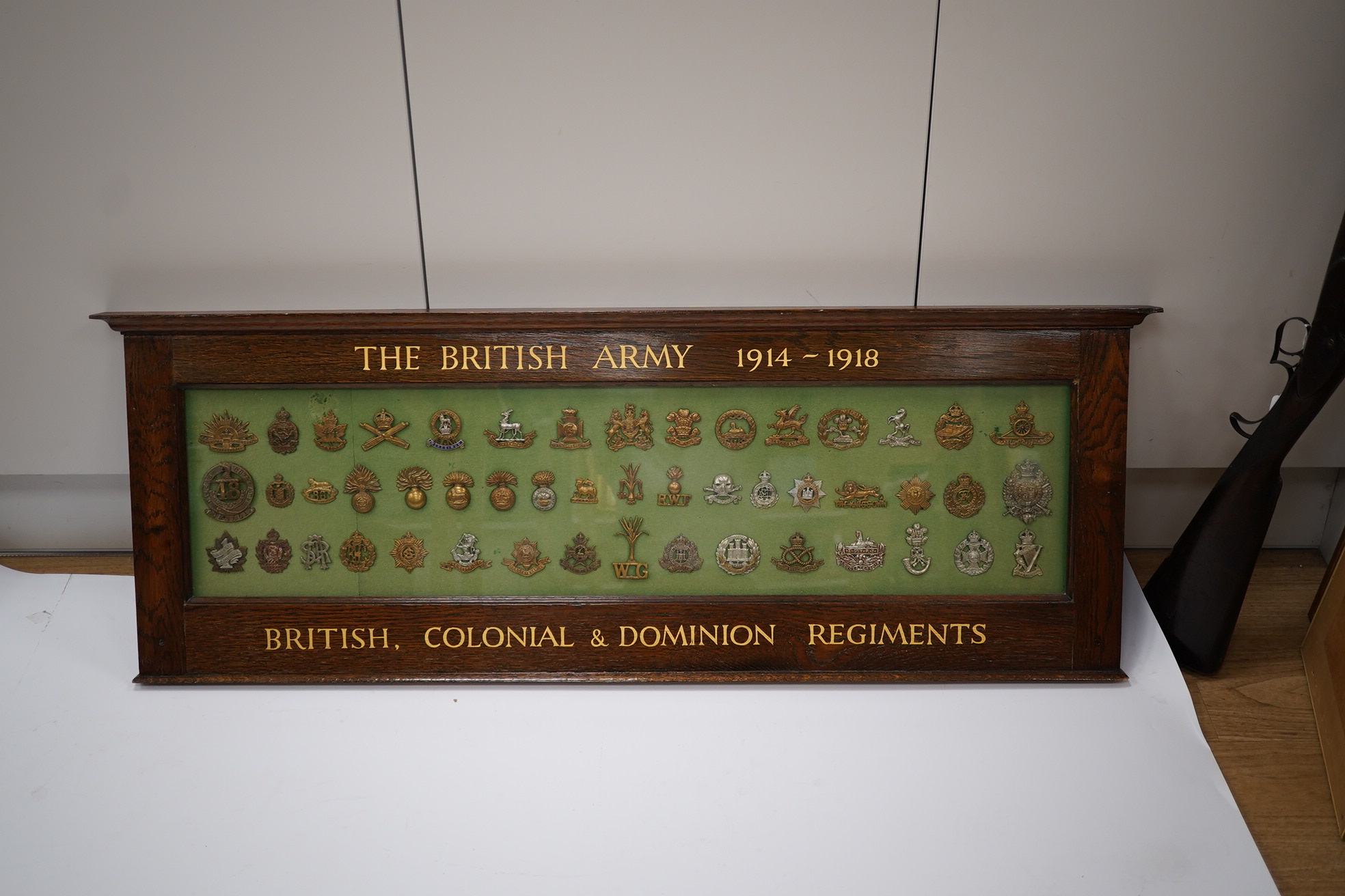 An oak framed display case of cap badges from the British, Colonial and Dominion Regiments, forty-nine badges including Australian Commonwealth Military Forces, the Royal Warwickshire Regiment, the Wiltshire Regiment, th